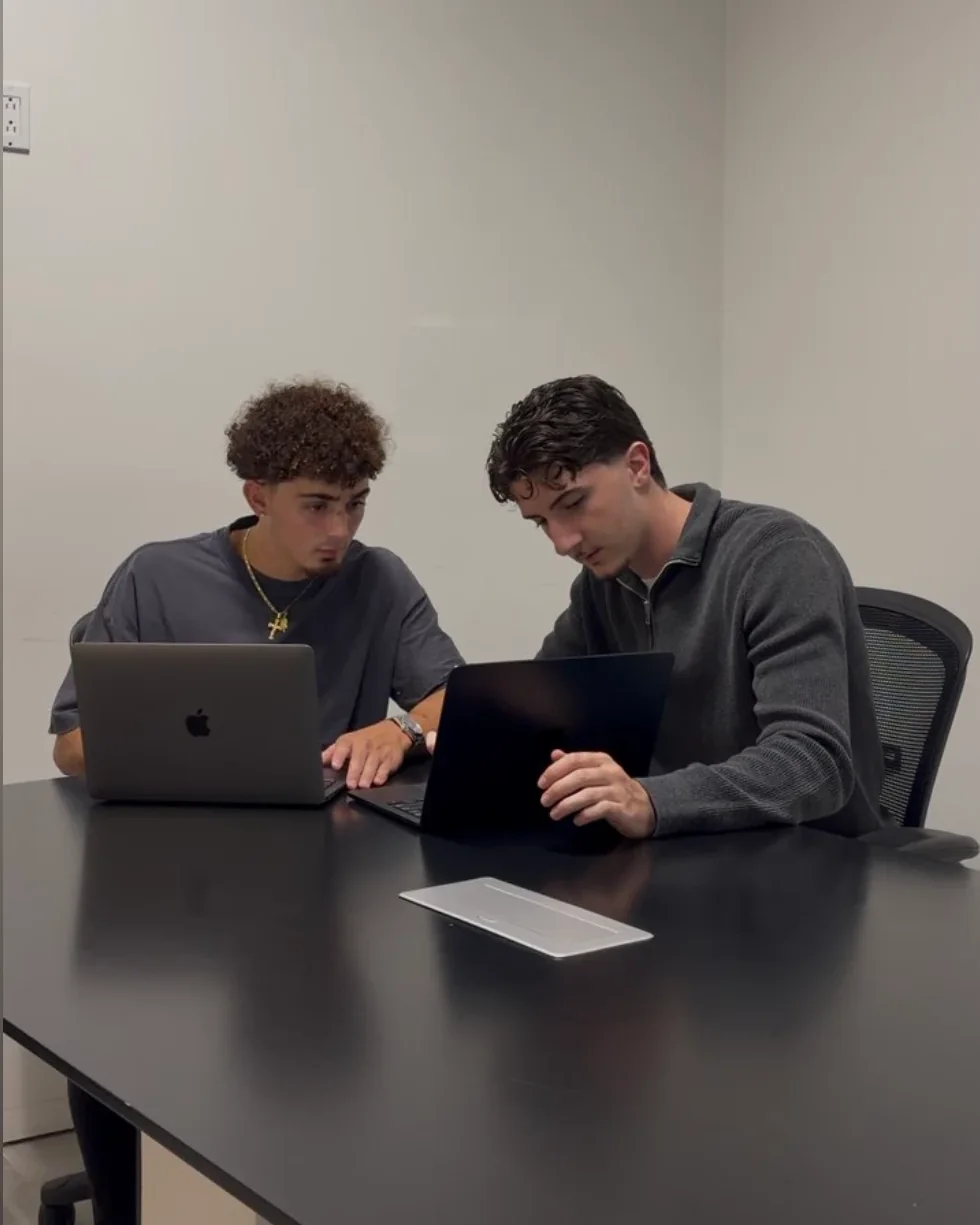 Luca Astorino, left, and Michael Pina, right, working side by side at a table on their laptops.